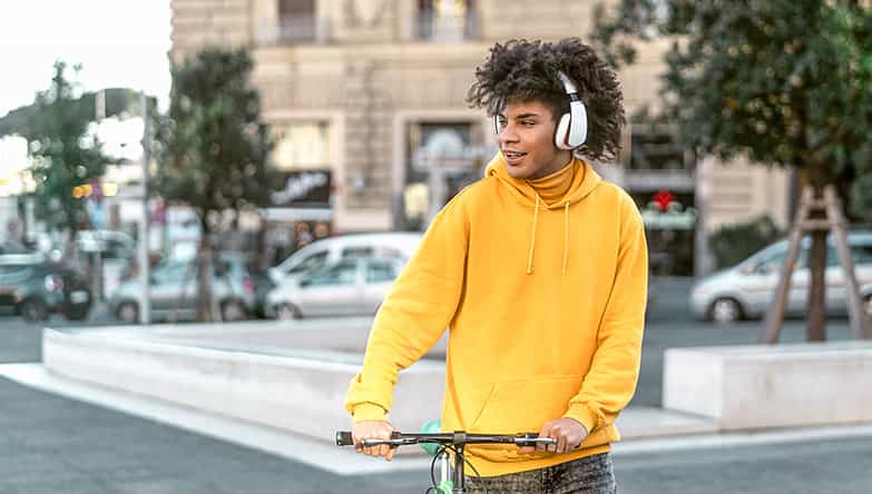 Ein Mann ist unterwegs mit dem Fahrrad in der Hand und hört Musik über seinen drahtlosen Kopfhörer.