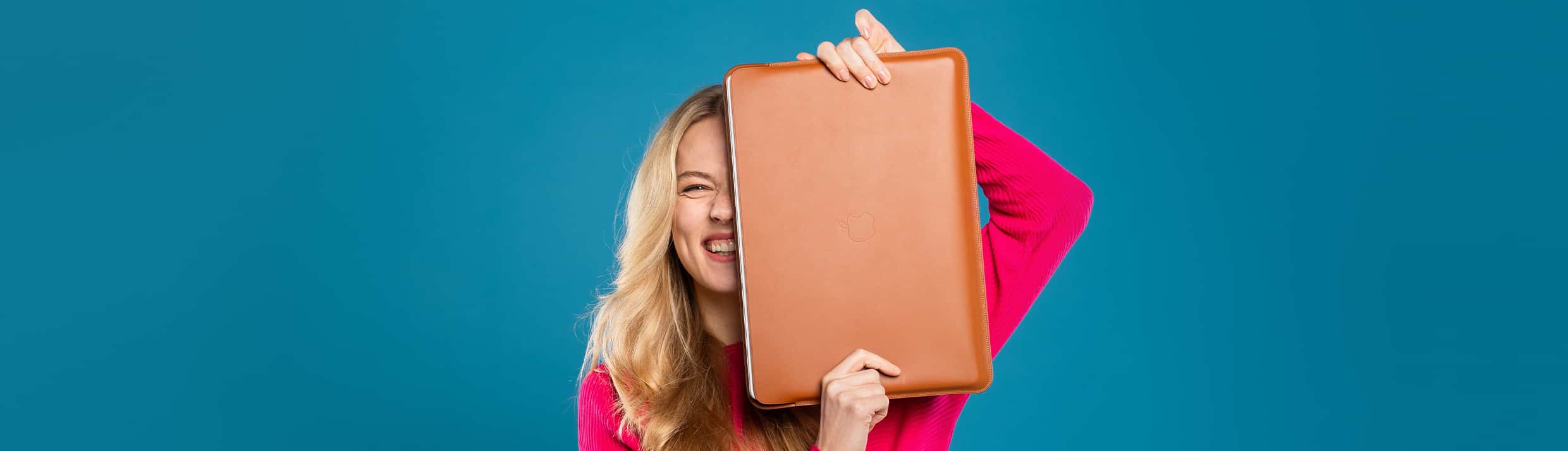 Eine Frau steht im Mittelpunkt, lächelnd mit einer Laptopsleeve oder Laptop-Hülle vor sich, in der ein Laptop geschützt ist.