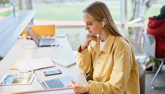 Eine Frau arbeitet an einem Schreibtisch und wird dank ihrer Noise-Cancelling-Ohrhörer nicht von ihrer Umgebung gestört.