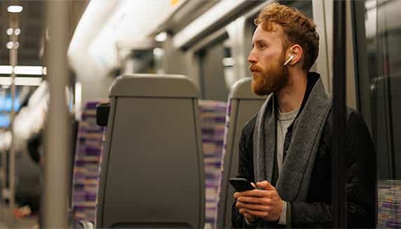 Ein Mann sitzt im Zug und hört über seine Ohrhörer seinen Podcast.