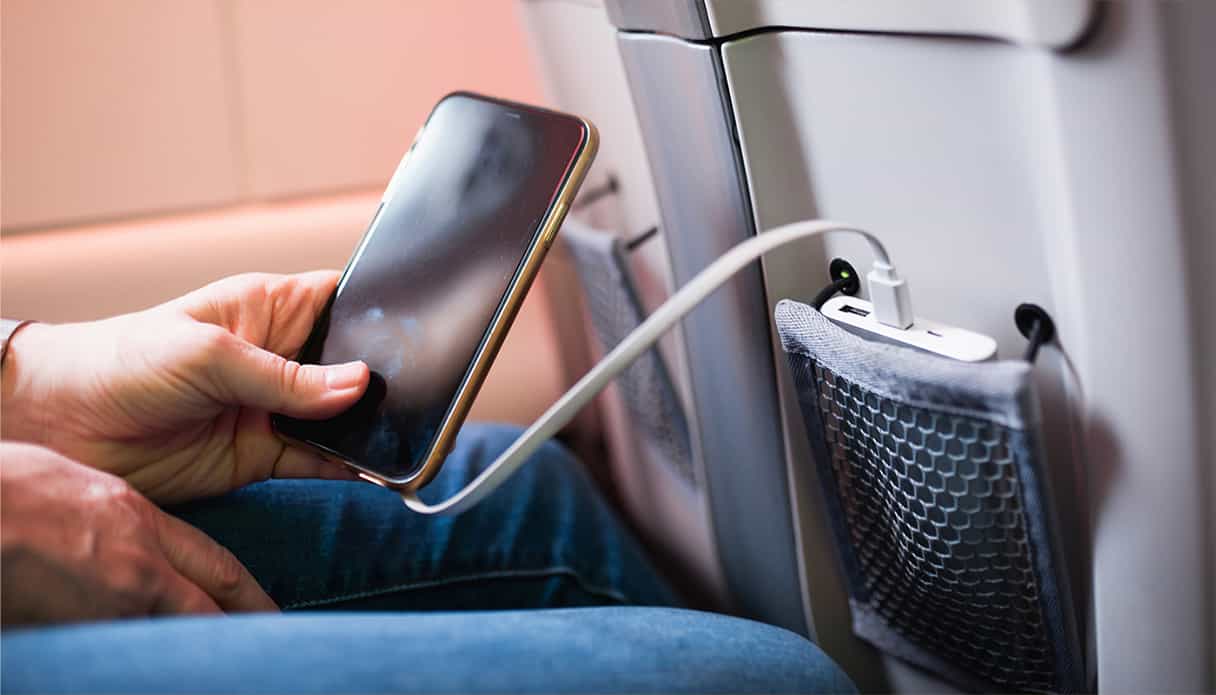 Das Telefon befindet sich in der Hand des Passagiers und ihre Powerbank liegt im Fach des Sitzes vor ihr.