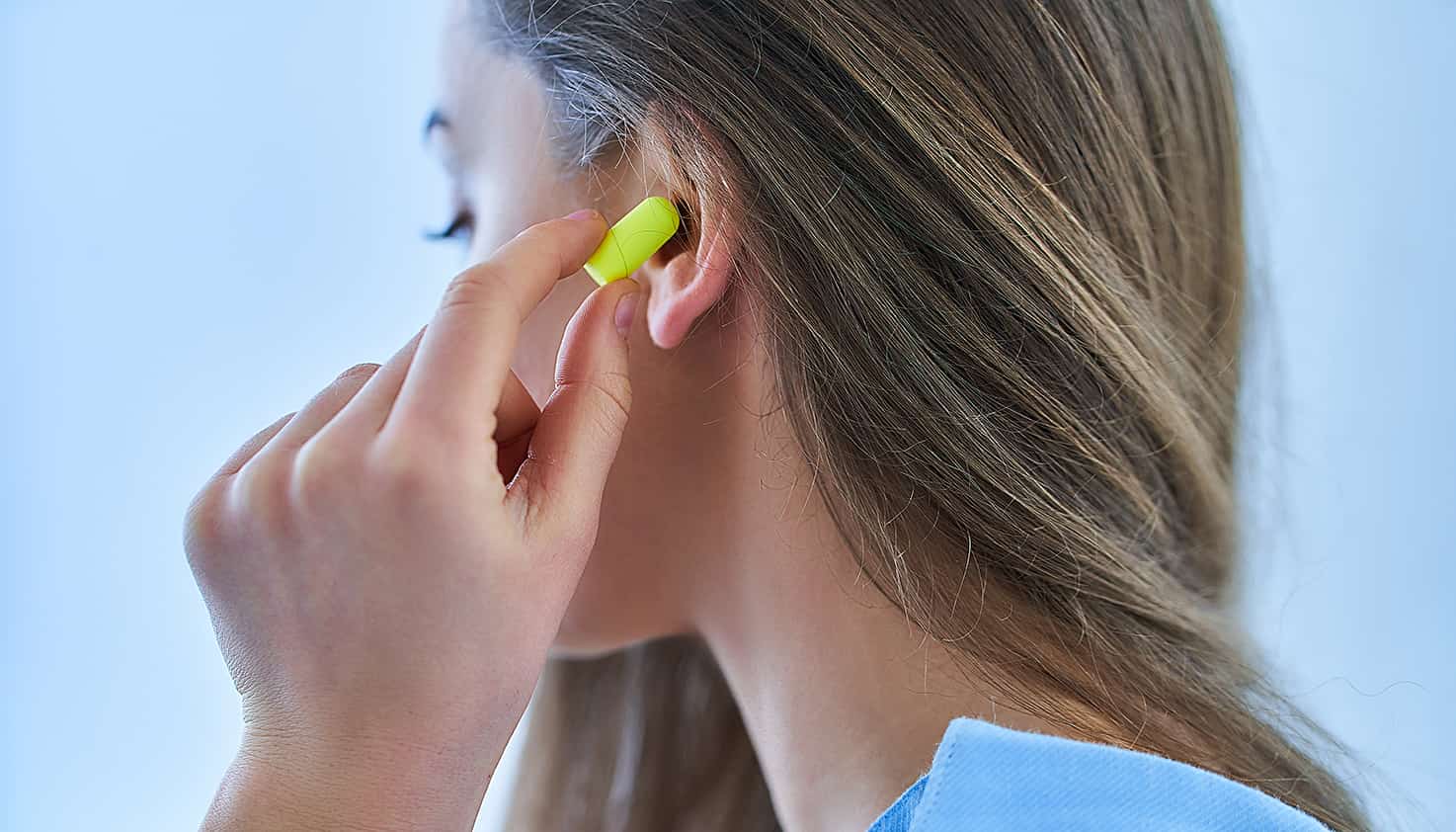 Eine Frau steckt sich gelbe Ohrstöpsel in ihr Ohr, um Gehörschäden auf dem Festival zu verhindern.