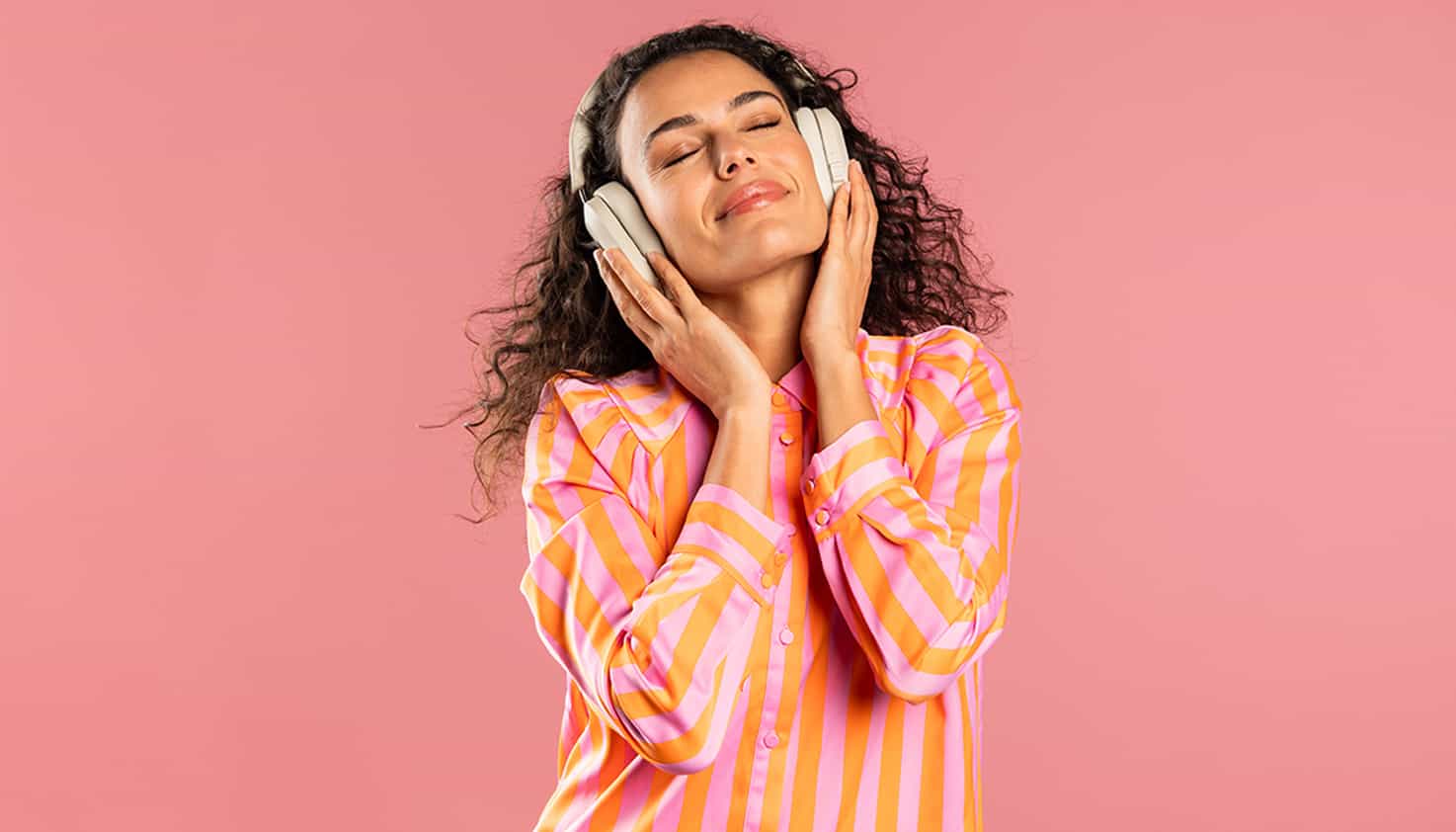 Eine Frau auf einem rosa Hintergrund genießt Musik mit geschlossenen Augen durch ihre geräuschunterdrückenden Kopfhörer.