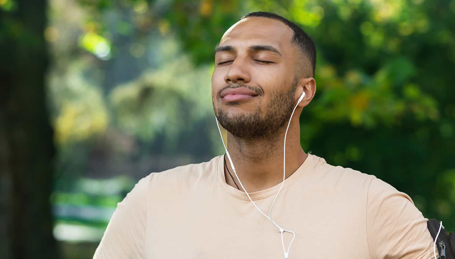 Der Mann atmet tief ein, während er im Park steht und seine Musik über seine verkabelten Ohrhörer hört.
