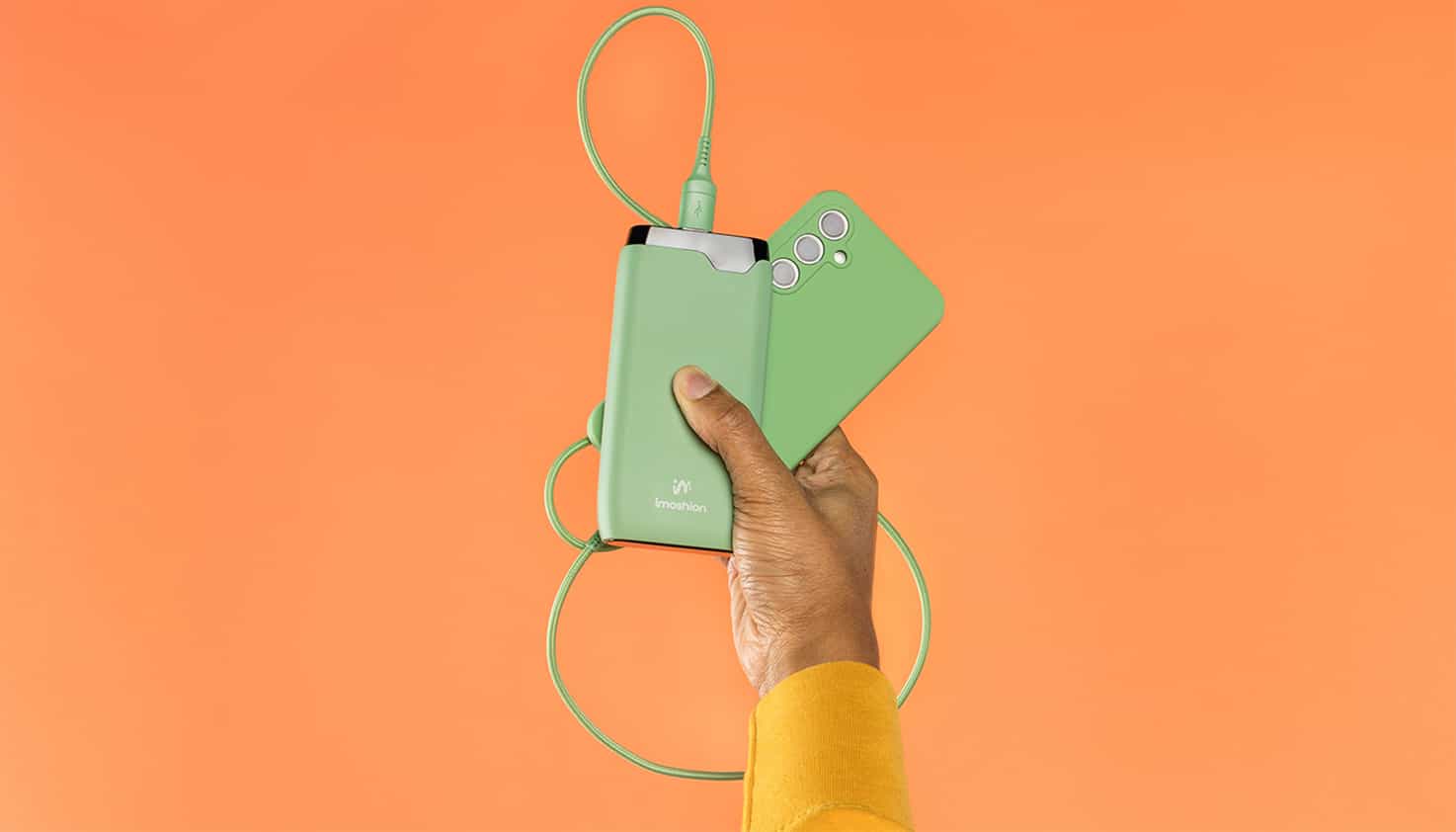 Eine knallorangefarbene Hintergrund mit einer auffällig grünen Powerbank und passendem Telefon.
