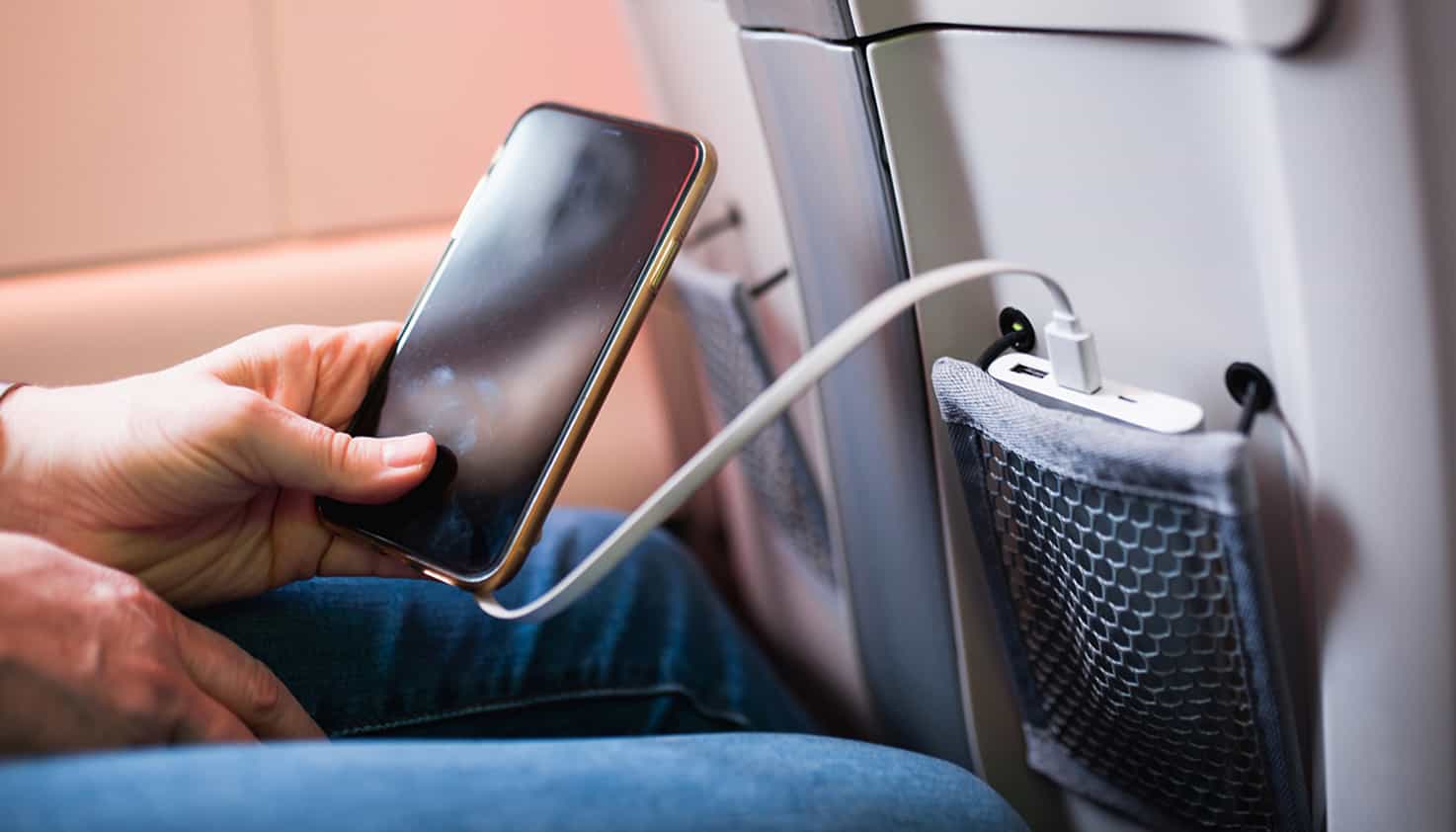 Das Telefon befindet sich in der Hand des Passagiers und ihre Powerbank liegt im Fach des Sitzes vor ihr.