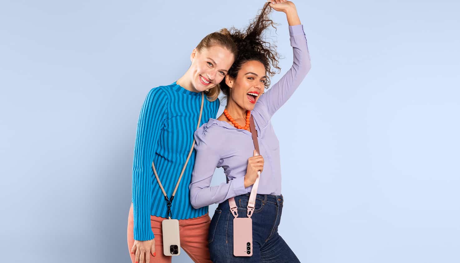 Zwei weibliche Models lächeln und tragen jeweils eine Handyhülle mit einem Band daran.