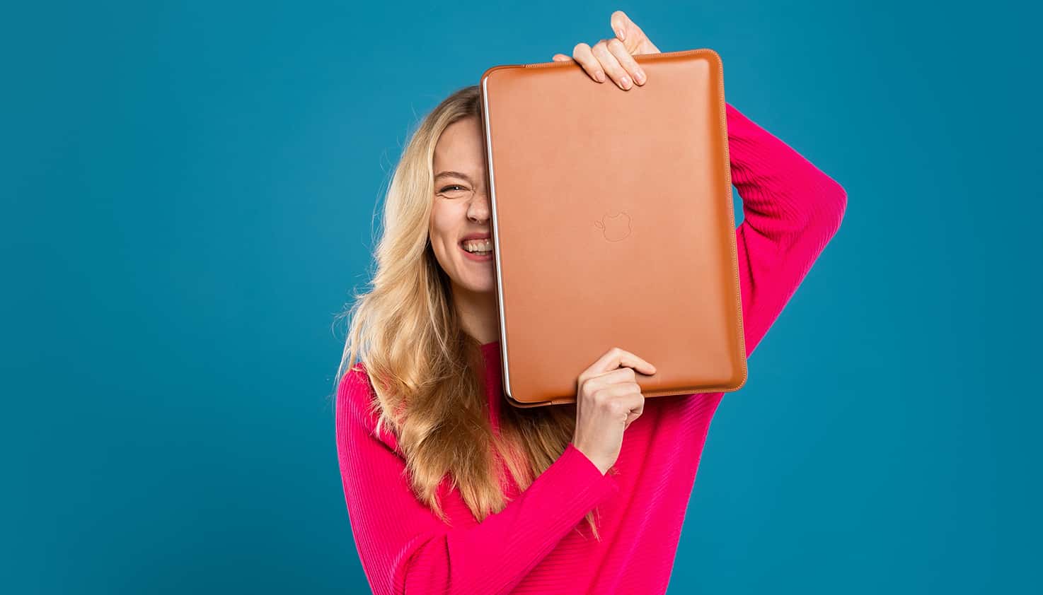 Eine Frau steht in der Mitte, lächelnd, mit einer Laptopsleeve oder -hülle vor sich, in der ein Laptop geschützt wird.