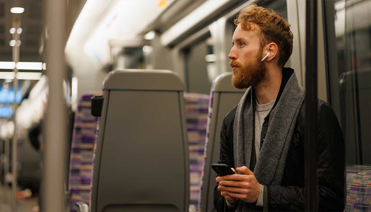 Ein Mann sitzt im Zug und hört über seine Ohrhörer seinen Podcast.